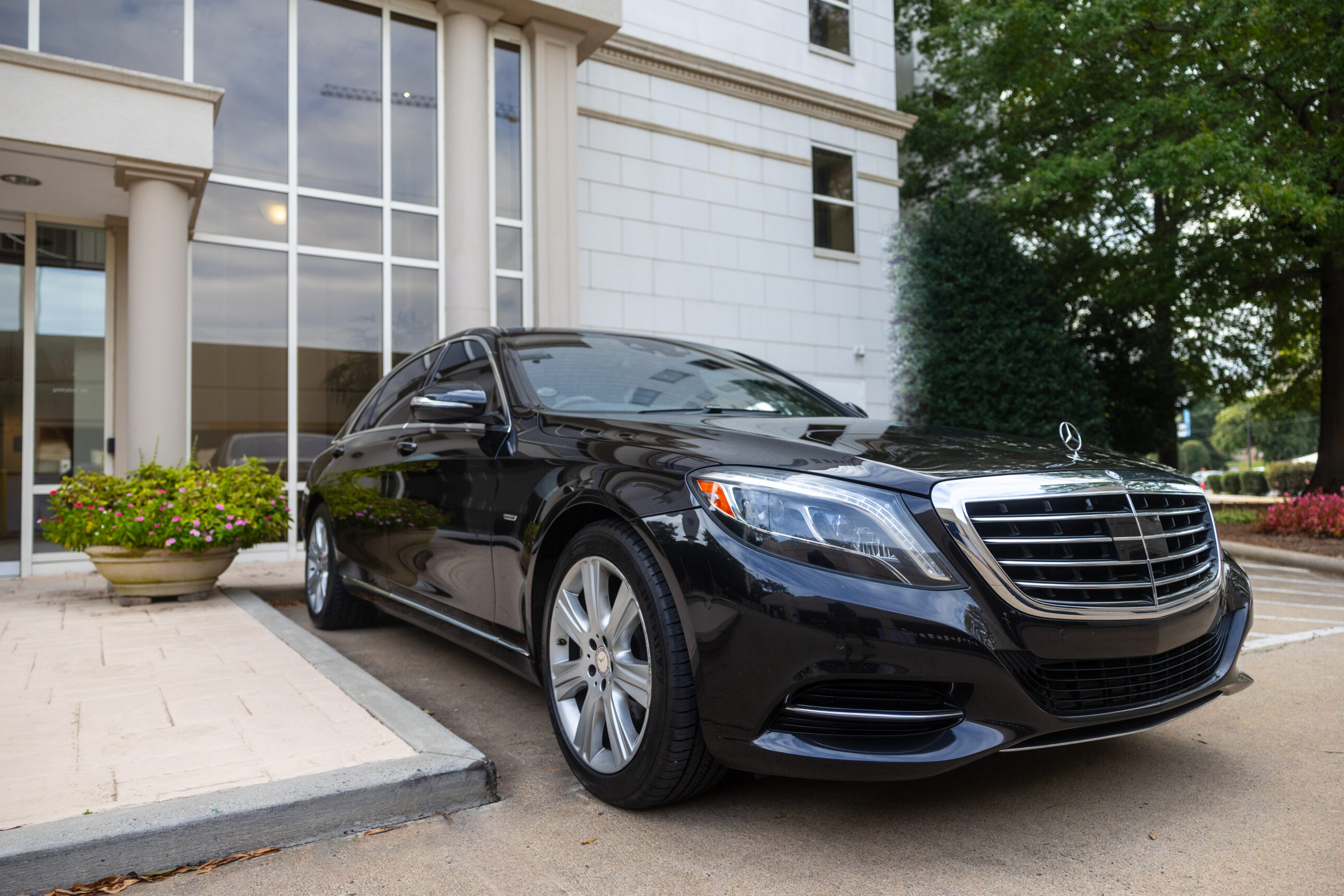 A Peak Black Mercedes S550 sedan parked outside a modern building, waiting to provide the best luxury car services for clients.