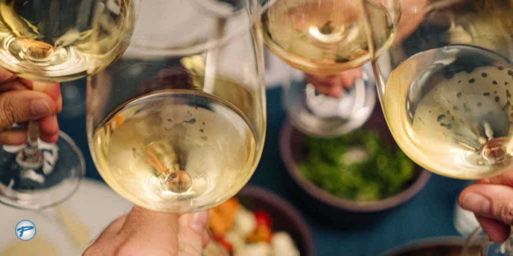 Group of friends clinking glasses of white wine at one of the vineyards near Charlotte, celebrating at a table filled with appetizers, representing what a gathering at Charlotte wineries could look like.