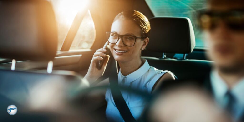 A professional woman speaking on the phone while seated comfortably in the backseat of a vehicle, highlighting chauffeur service and executive car transportation for business and luxury travel needs.