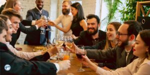 A group of friends and colleagues clink glasses at a festive gathering, smiling and enjoying the celebration around a table of drinks and appetizers. The image emphasizes the convenience of party transportation and bus rental services for safely transporting groups to events.