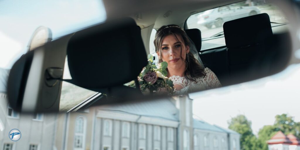 A bride's reflection in a car's rearview mirror captures her anticipation on her wedding day. A perfect moment of wedding day transportation.