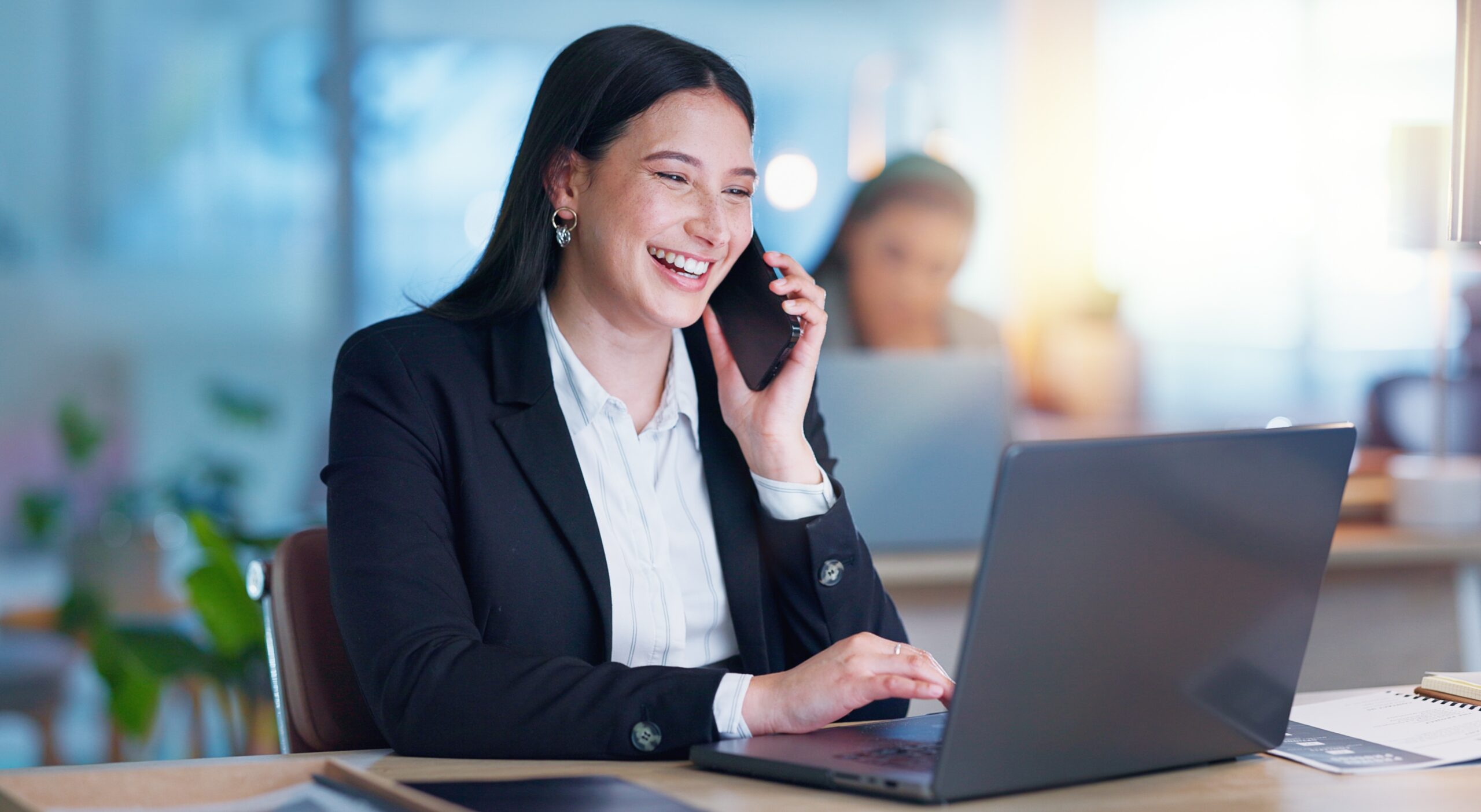 Smiling professional coordinating group transportation services on a phone call, managing group event transportation logistics from her laptop.